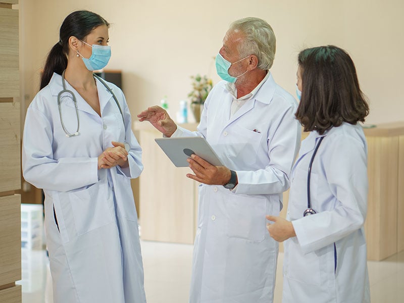 group-of-diverse-medical-doctor-team-wearing-surgical-face-mask-talking-and-consoling-with-Tablet-Computer-in-hospital